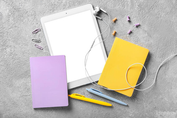 Stationery supplies, tablet computer and earphones on grey background