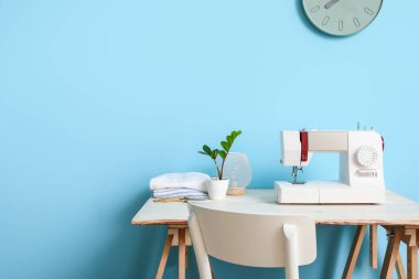 Mavi duvarın yanında dikiş makinesi olan bir terzi.