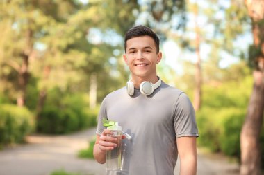 Parkta su ve kulaklık şişesi olan genç bir adam.