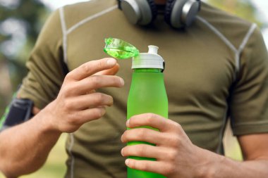 Sportif genç adam parkta su şişesini açıyor, yakın plan.
