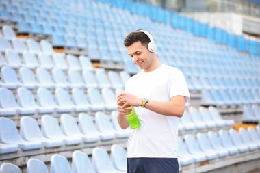 Sportif genç adam stadyumda su şişesi açıyor.