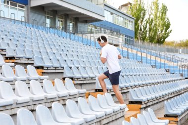 Stadyumun üst katında kulaklıklı genç bir adam koşuyor.