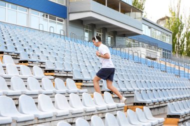 Stadyumun üst katında kulaklıklı genç bir adam koşuyor.