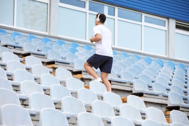 Stadyumun üst katında kulaklıklı genç bir adam koşuyor.