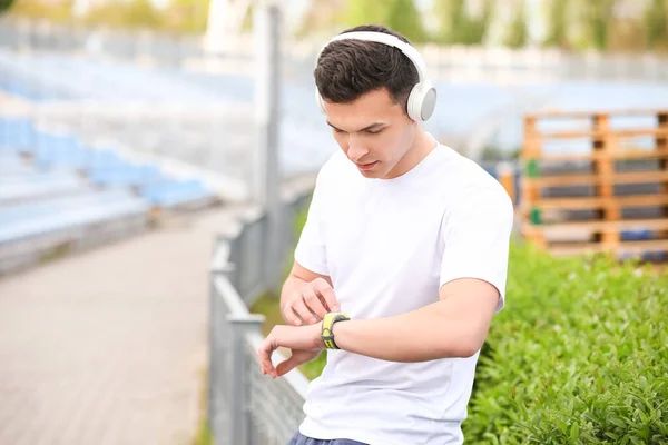 Sporty young man checking pulse at stadium