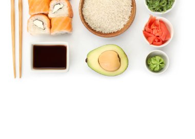 Lezzetli suşi ruloları, soya soslu kase, yemek çubukları ve beyaz arka planda malzemeler.