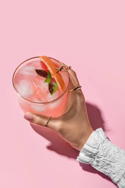 Renkli arka planda bir bardak lezzetli greyfurt margaritası tutan kadın, yakın plan.