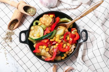 Farklı sebzelerle kızartma tavası ve hafif arka planda baharatlar.