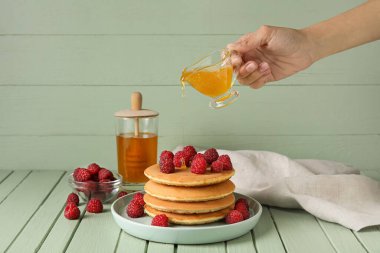 Kadın, ahşap arka planda lezzetli kreplerle tabağa bal döküyor.