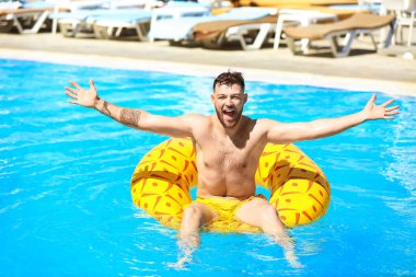 Yüzme havuzunda şişme yüzüğü olan genç bir adam.