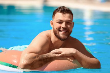 Yüzme havuzunda şişme yüzüğü olan genç bir adam.