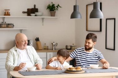 Mutlu adam, küçük oğlu ve babası mutfakta kahvaltı yapıyor.