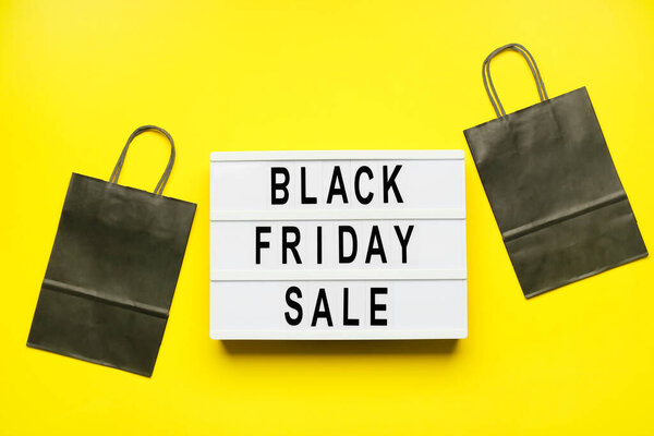 Shopping bags and board with text BLACK FRIDAY SALE on color background