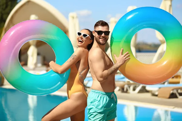 Young couple with inflatable rings near swimming pool