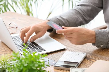 Bilgisayarı ve kredi kartı olan bir iş adamı iş yerinde oturuyor.