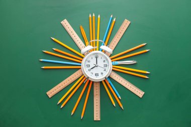 Yeşil arkaplanda kırtasiye malzemesi olan çalar saat