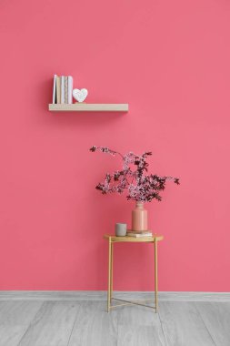 Kitap rafı ve çiçek açan dallar renk duvarının yanındaki masada.