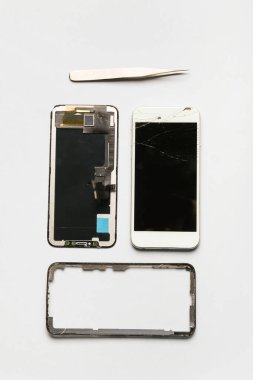 Parçalanmış cep telefonu ve beyaz arkaplanda cımbızlar