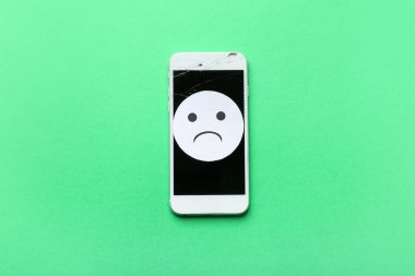 Bozuk ekranlı cep telefonu ve yeşil arka planda üzgün bir gülümseme.