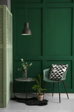 Yeşil oturma odasının içindeki sandalyenin yanındaki masada şık cam vazo.