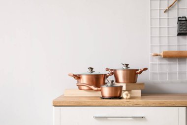 Işık duvarının yanındaki tezgahta bakır tencereler var.