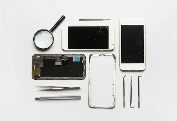 Disassembled mobile phone, technician tools and magnifier on white background