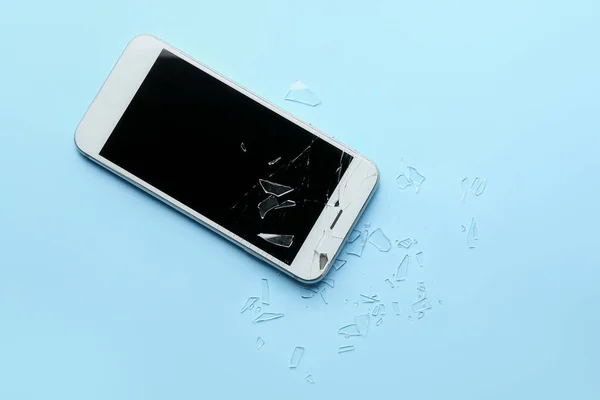 Mobile phone with broken screen and pieces of glass on color background