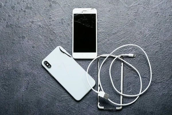 Broken mobile phones and charging cord on dark background