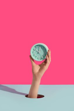 Çalar saati renk arkaplanındaki delikten geçiren kadın eller