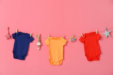 Farklı bebek kıyafetleri ve pembe arka planda asılı duran oyuncaklar.