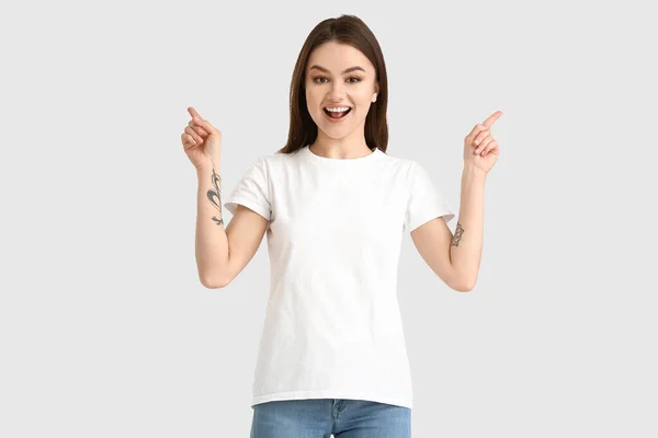 Modern Tişörtlü Genç Kadın Beyaz Arka Plandaki Bir Şeyi Işaret — Stok fotoğraf