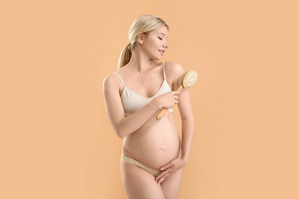 美しいです妊娠中の若いです女性とともにマッサージブラシ上の色背景 — ストック写真