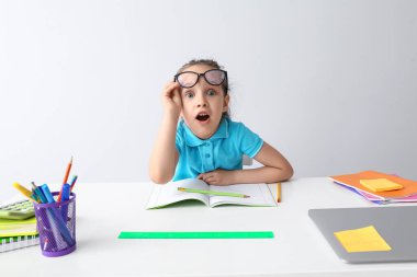 Şok olmuş küçük bir kız, masa arkasında ödevlerini yapıyor.