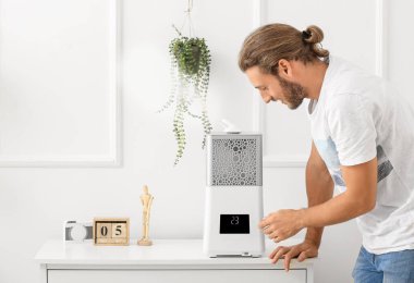 Genç adam evdeki modern nemlendiriciyi açıyor.