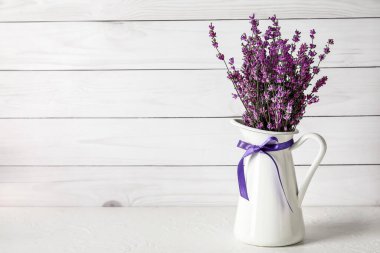 Hafif ahşap arka planda güzel lavanta çiçekleri olan bir sürahi.