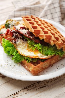 Hafif ahşap arka planda yumurta, pastırma ve sebzeli leziz Belçika waffle 'ları.