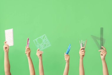 Yeşil arka planda okul malzemeleri olan birçok farklı el.