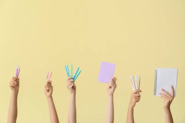 Renkli arka planda okul malzemesi olan birçok farklı el.