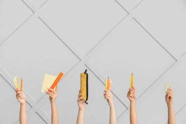 Birçok farklı el ve gri duvar arkasında okul malzemeleri var.