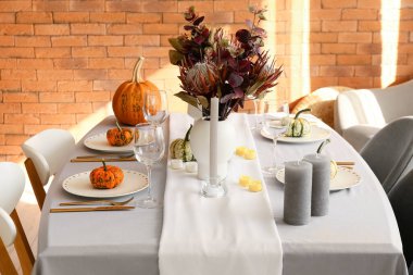 Tuğla duvarın yanında balkabaklı ve çiçekli yemek masası.