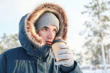 Karlı bir günde elinde bir fincan sıcak çayla genç bir adam