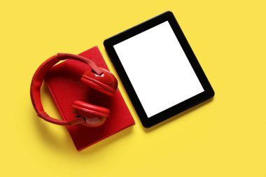 Modern tablet bilgisayar, kulaklık ve sarı arkaplan üzerine kitap