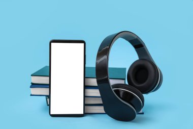 Modern cep telefonu, kulaklık ve mavi arka plan kitapları.