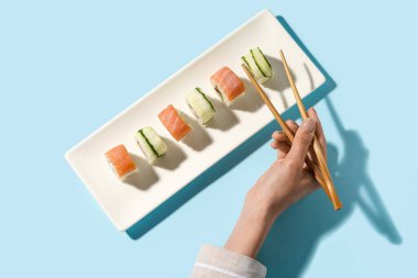 Kadın, arka plandaki tabaklardan suşi topluyor.