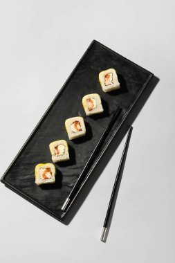 Nefis suşi ruloları ve hafif arka planda yemek çubukları olan bir tabak.