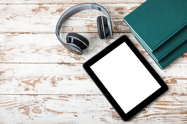 Modern tablet computer, headphones and books on light wooden background