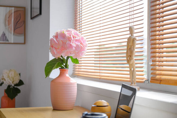 Ваза с цветами гортензии на столе и деревянный манекен у окна