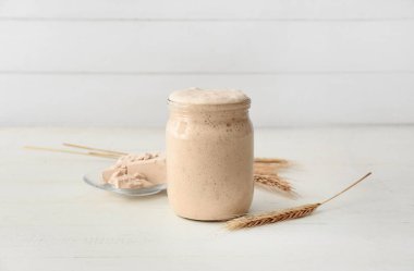 Taze ekşi mayalı cam kavanoz ve beyaz ahşap arka planda dikenler.