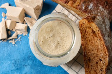 Mavi arka planda taze mayalı cam kavanoz ve ekmek.