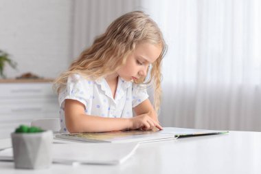 Evde kitap okuyan sevimli küçük bir kız.